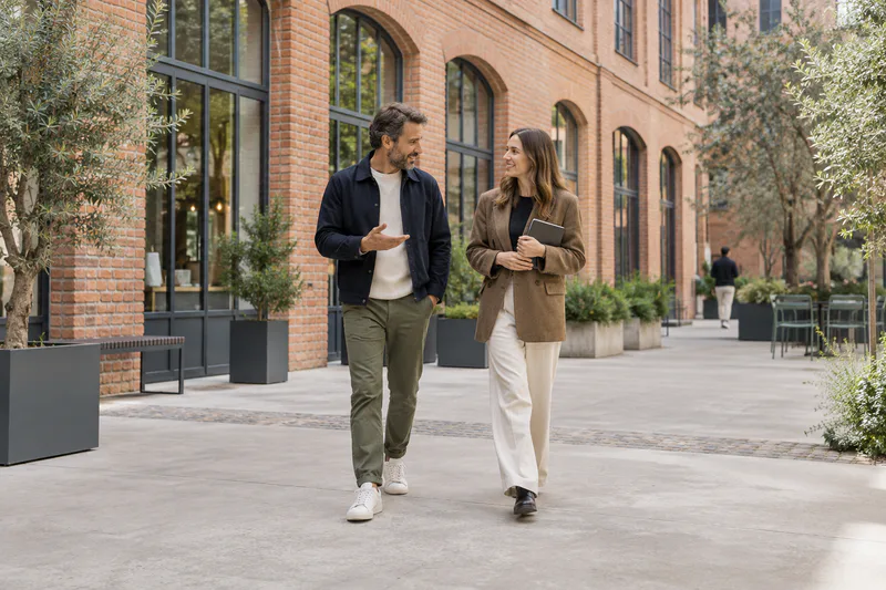 Two people talk as they walk through the courtyard of a renovated brick building.